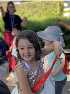 Children dancing outdoors, trailing red ribbons