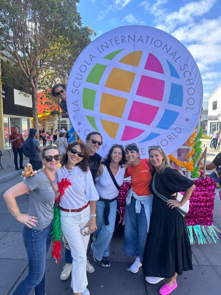 Parents posing together at an outdoor event beside a large La Scuola globe sign